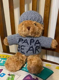 a crocheted teddy bear wearing a sweater and hat