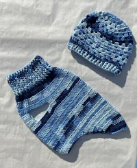 a blue crocheted sweater and hat on a white surface